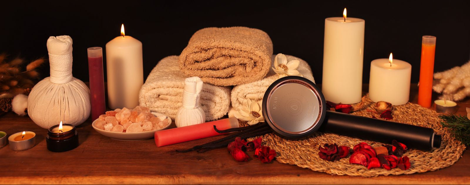 SOAH Black Edition shower head with spa setup including candles, towels, and bath salts on a wooden surface with a dark background.